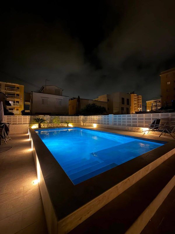 Piscina de obra elevada de noche con iluminación LED azul en el vaso y luces en el perímetro
