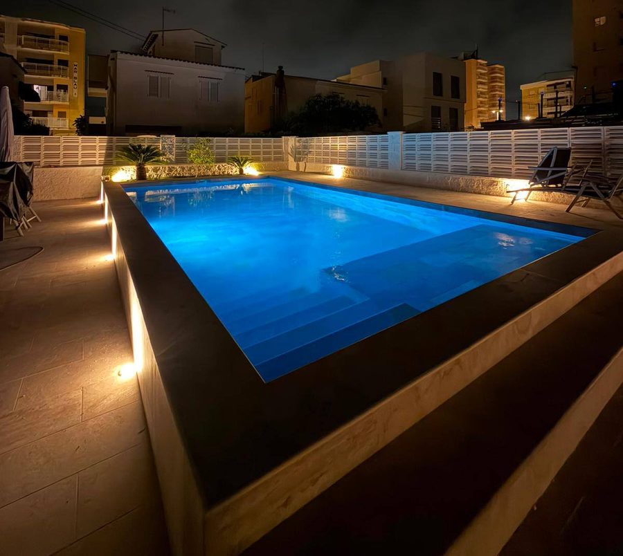 Piscina de obra elevada de noche con iluminación LED azul en el vaso y luces en el perímetro