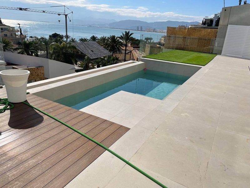 Piscina de obra en una terraza con escalón integrado, coronación y pavimento porcelánico claro y tarima de composite